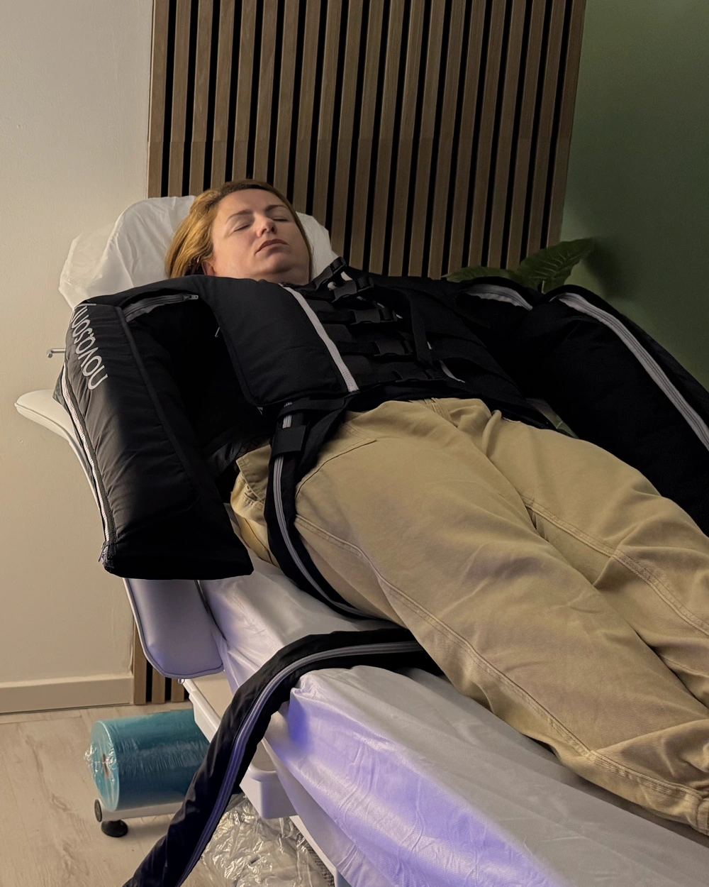 ענת בחליפת הטיפול בחדר של Anat Massage, לצד חיפוי העץ והקיר הירוק